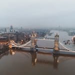 Drone view of London city located in England with illuminated Tower Bridge on River Thames near buildings in misty weather under gray cloudy sky in daylight